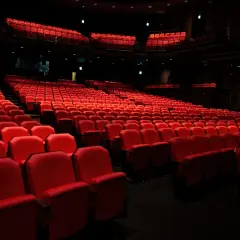 Puste czerwone fotele w teatrze, czekające na widzów. Zastanawiasz się, ile trwa spektakl w teatrze?