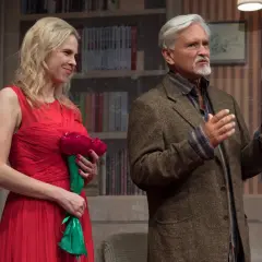 Aktorzy na scenie, kobieta w czerwonej sukni z bukietem, mężczyzna w tweedowej marynarce. Spektakl "Edukacja Rity" w teatrze.
