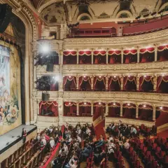 Widownia teatru w Krakowie, gdzie warto iść na spektakl. Złote zdobienia, czerwone aksamitne obicia i wielki malowany kurtyna tworzą magiczną atmosferę.