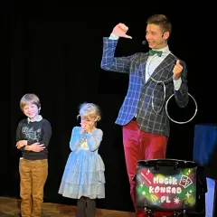 Magik Konrad wyjaśnia dzieciom, co to jest teatr, podczas pokazu iluzji. Dzieci z zaciekawieniem obserwują sztuczki.