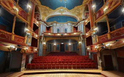 Wnętrze teatru z czerwonymi fotelami i złotymi zdobieniami. Idealne miejsce na wieczorne wyjście na spektakl, na co do teatru w Łodzi.