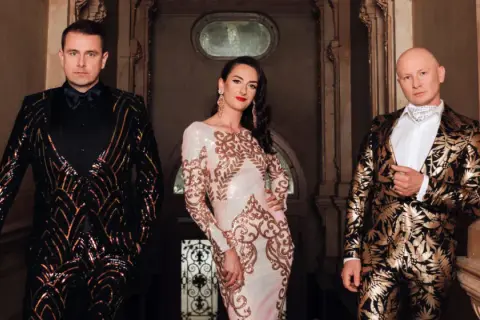 Kabaret K2 skład: mężczyzna w błyszczącej marynarce, kobieta w sukni z cekinami i mężczyzna w złotej marynarce.