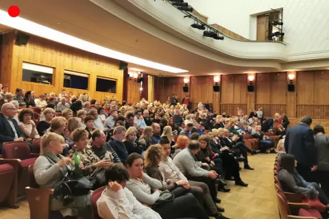 Widownia w teatrze, ludzie siedzą w rzędach, ubrani elegancko.