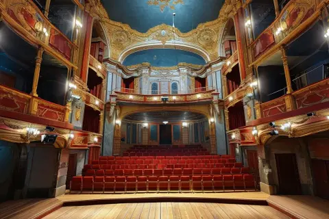 Wnętrze teatru z czerwonymi fotelami i złotymi zdobieniami. Idealne miejsce na wieczorne wyjście na spektakl, na co do teatru w Łodzi.