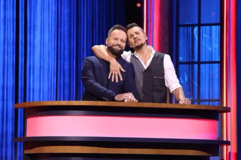 Michał Czernecki i jego kolega z kabaretu, w objęciach, na scenie z niebieską kurtyną w tle.