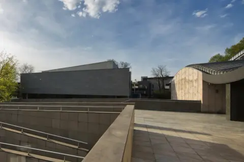 Nowoczesna architektura muzeum sztuki i techniki japońskiej Manggha z kamiennymi fasadami i zielenią w tle.