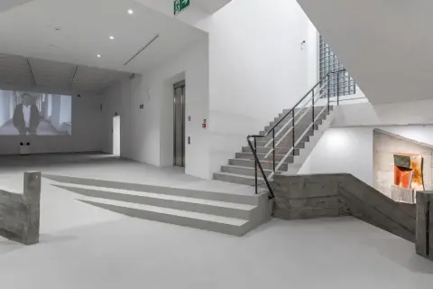 Wnętrze muzeum sztuki współczesnej Kraków: projekcja wideo, betonowe schody i rzeźba.