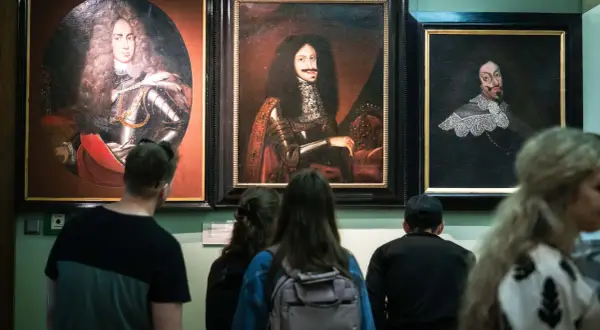Zwiedzający podziwiają portrety w muzeum sztuki Wrocław. Widać barokowe stroje i peruki.