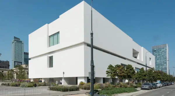 Nowoczesny budynek Muzeum Sztuki Nowoczesnej w Warszawie, projekt architektoniczny o białej fasadzie, na tle błękitnego nieba.