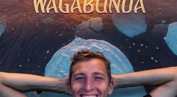 Uśmiechnięty Piotr Szumowski, gwiazda stand-upu, leży na tle napisu "WAGABUNDA" i lodowych krajobrazów.