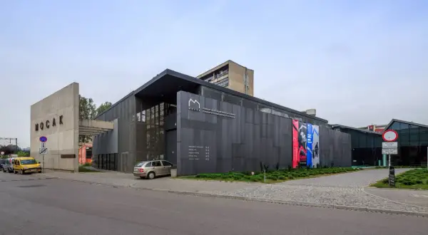 Nowoczesny budynek MOCAK Muzeum Sztuki Współczesnej w Krakowie z betonowym napisem i szarymi panelami.