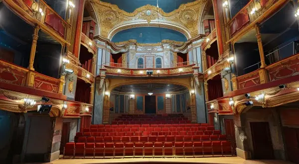 Wnętrze teatru z czerwonymi fotelami i złotymi zdobieniami. Idealne miejsce na wieczorne wyjście na spektakl, na co do teatru w Łodzi.