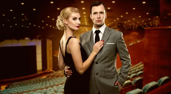 Elegancka kobieta w czarnej sukni i mężczyzna w garniturze, idealnie ubrani do teatru muzycznego.