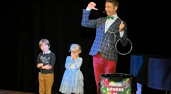 Magik Konrad wyjaśnia dzieciom, co to jest teatr, podczas pokazu iluzji. Dzieci z zaciekawieniem obserwują sztuczki.