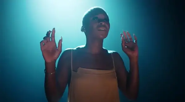 Cynthia Erivo stand up, wznosi ręce w górę, w świetle reflektorów.