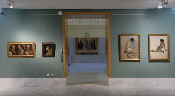 Wnętrze muzeum sztuk pięknych w Walencji. Obrazy wiszą na zielonych ścianach, a marmurowa podłoga odbija światło.