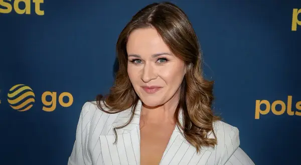 Ewa Błachnio, znana z kabaretów, w białej marynarce w prążki, uśmiecha się do obiektywu.
