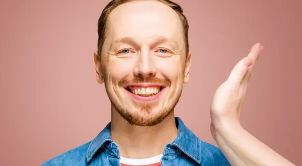 Uśmiechnięty mężczyzna w dżinsowej koszuli, jakby właśnie usłyszał świetny żart na występie syrek dąbrowski stand up.