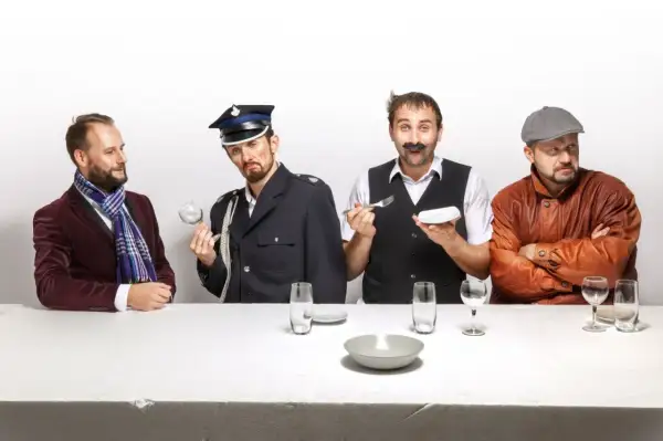 Czterech panów przy stole, jeden w garniturze, drugi w mundurze, trzeci z wąsami i sztućcami, czwarty w skórzanej kurtce. Scena jak z kabaretu z Kielc.
