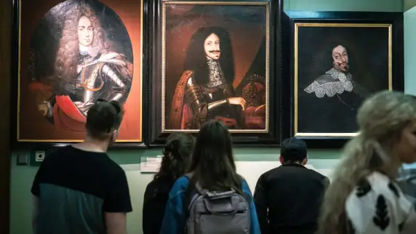 Zwiedzający podziwiają portrety w muzeum sztuki Wrocław. Widać barokowe stroje i peruki.