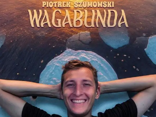 Uśmiechnięty Piotr Szumowski, gwiazda stand-upu, leży na tle napisu "WAGABUNDA" i lodowych krajobrazów.