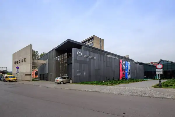 Nowoczesny budynek MOCAK Muzeum Sztuki Współczesnej w Krakowie z betonowym napisem i szarymi panelami.