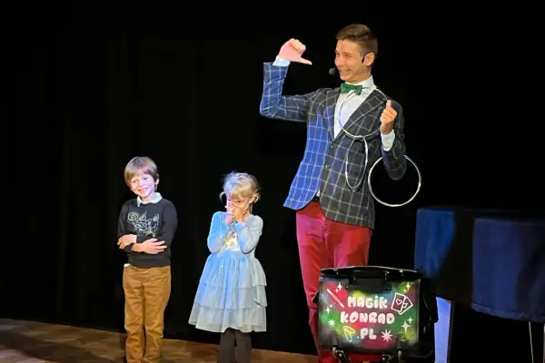 Magik Konrad wyjaśnia dzieciom, co to jest teatr, podczas pokazu iluzji. Dzieci z zaciekawieniem obserwują sztuczki.