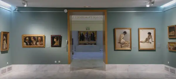 Wnętrze muzeum sztuk pięknych w Walencji. Obrazy wiszą na zielonych ścianach, a marmurowa podłoga odbija światło.
